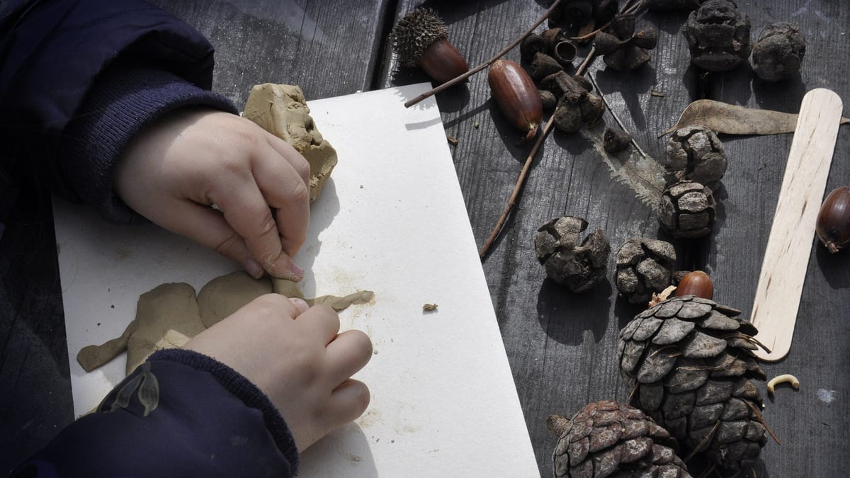 Enfant façonnant de l'argile près de pommes de pin et de glands