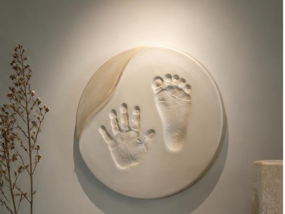 Médaillon rond en argile crème portant l'empreinte de la main et du pied d'un bébé